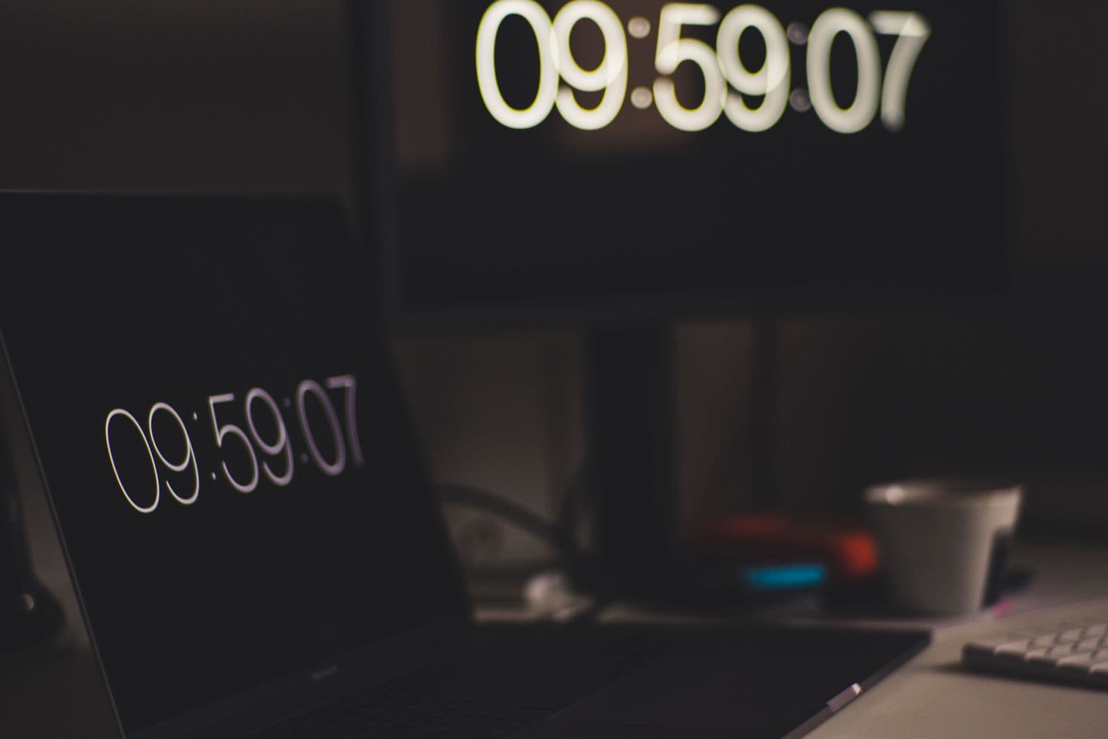 Digital time display on a laptop screen, with the same time shown on a larger screen in the background