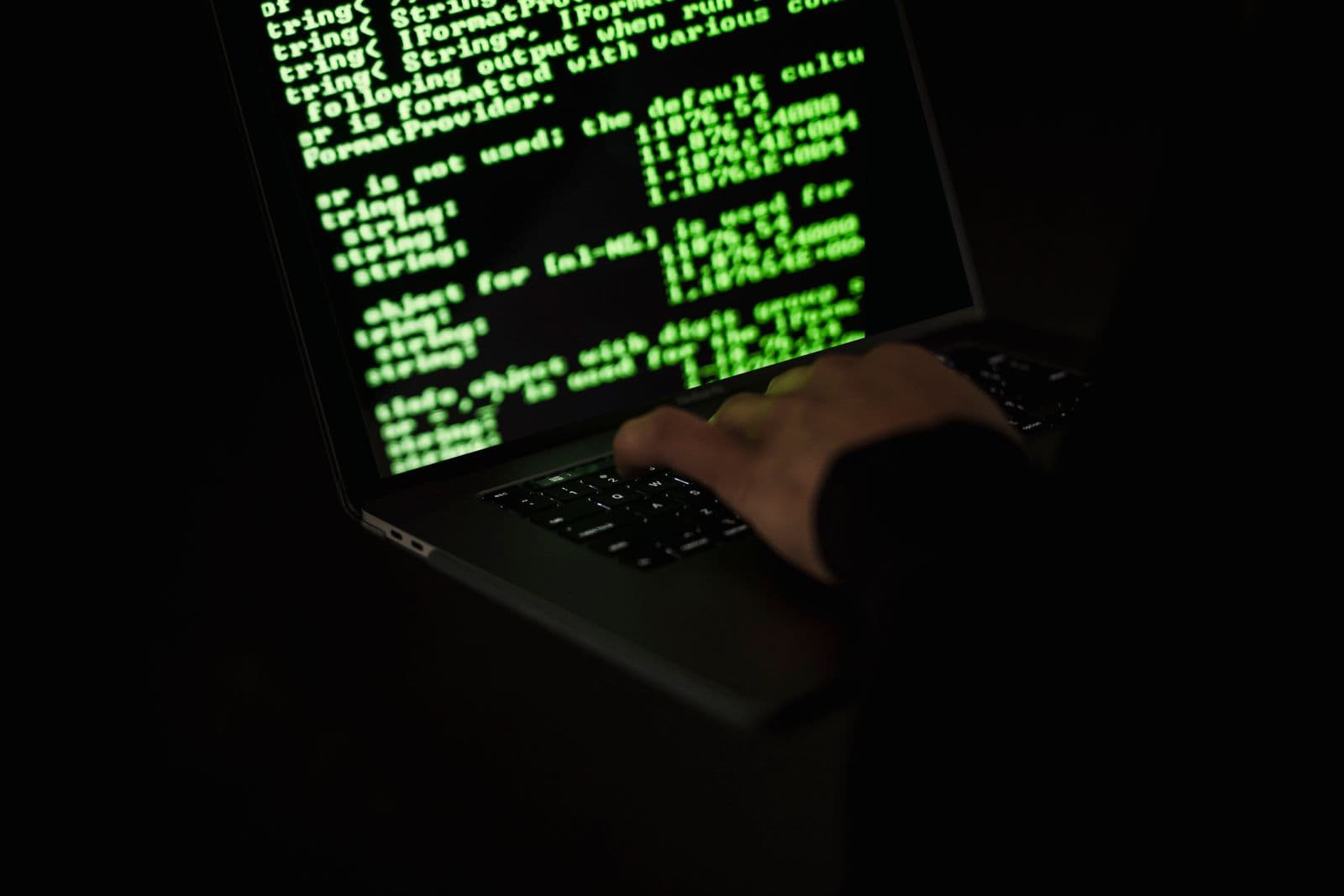 Close-up of a laptop screen showing green terminal text, with a hand resting on the keyboard