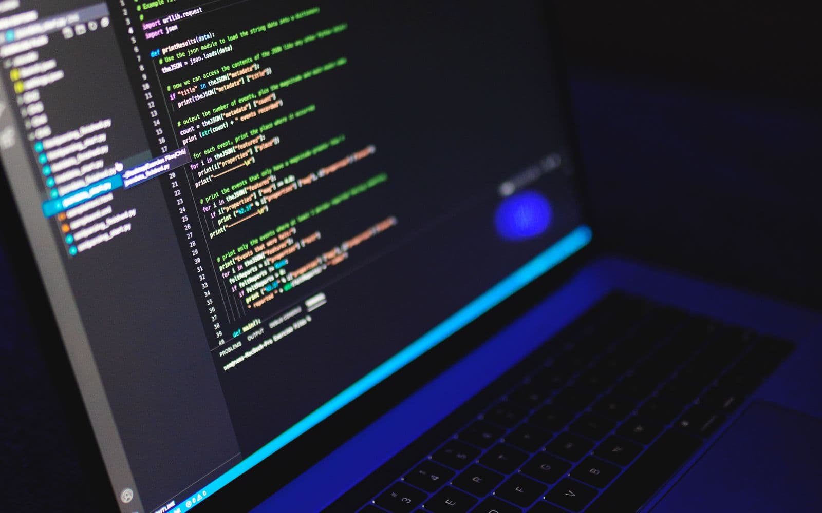 Aufgeklappter Laptop, auf dem Bildschirm farbig hervorgehobener Programmcode in einem dunklen Raum