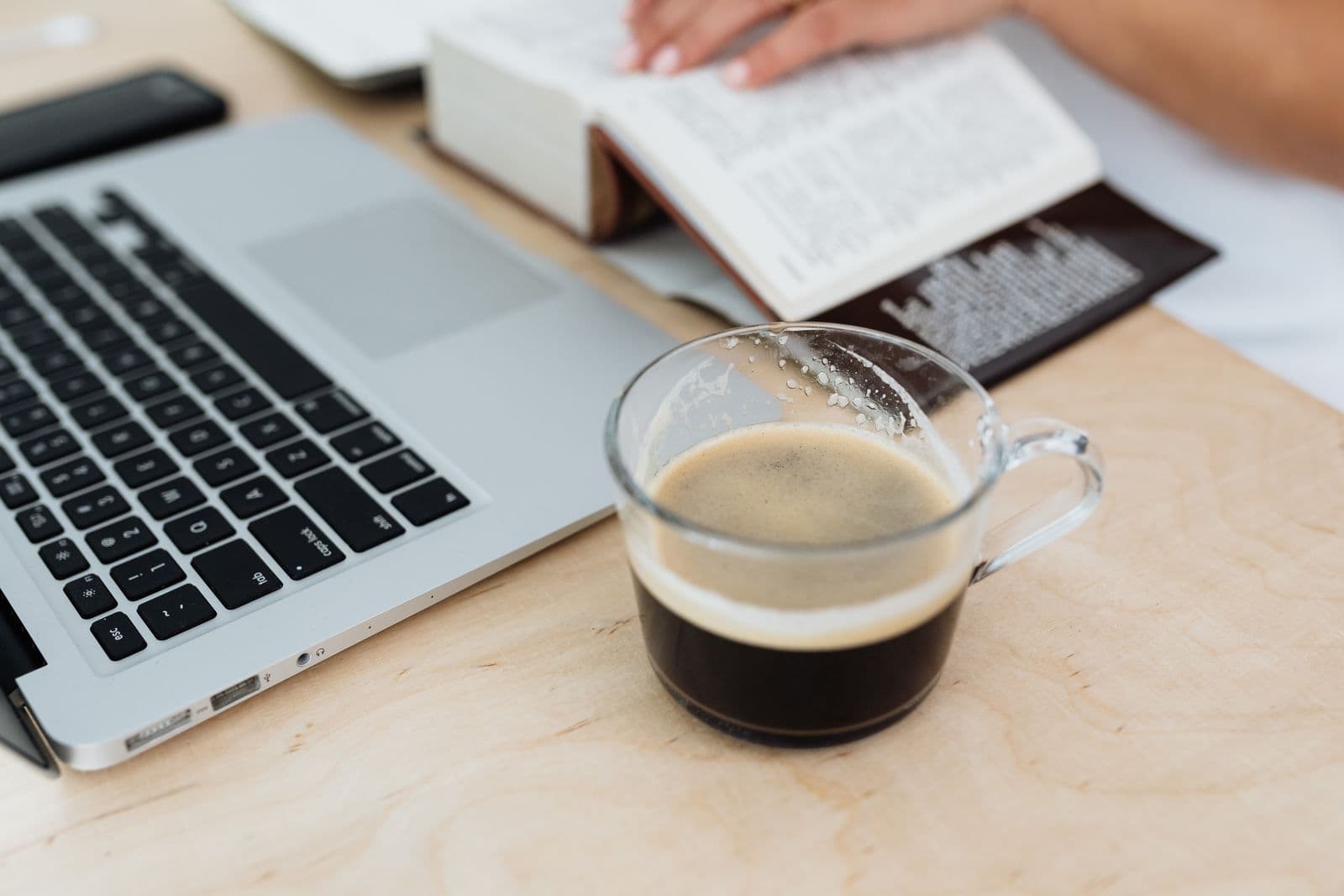 Arbeitsplatz mit Laptop, Buch und Kaffeetasse auf einem Holzschreibtisch