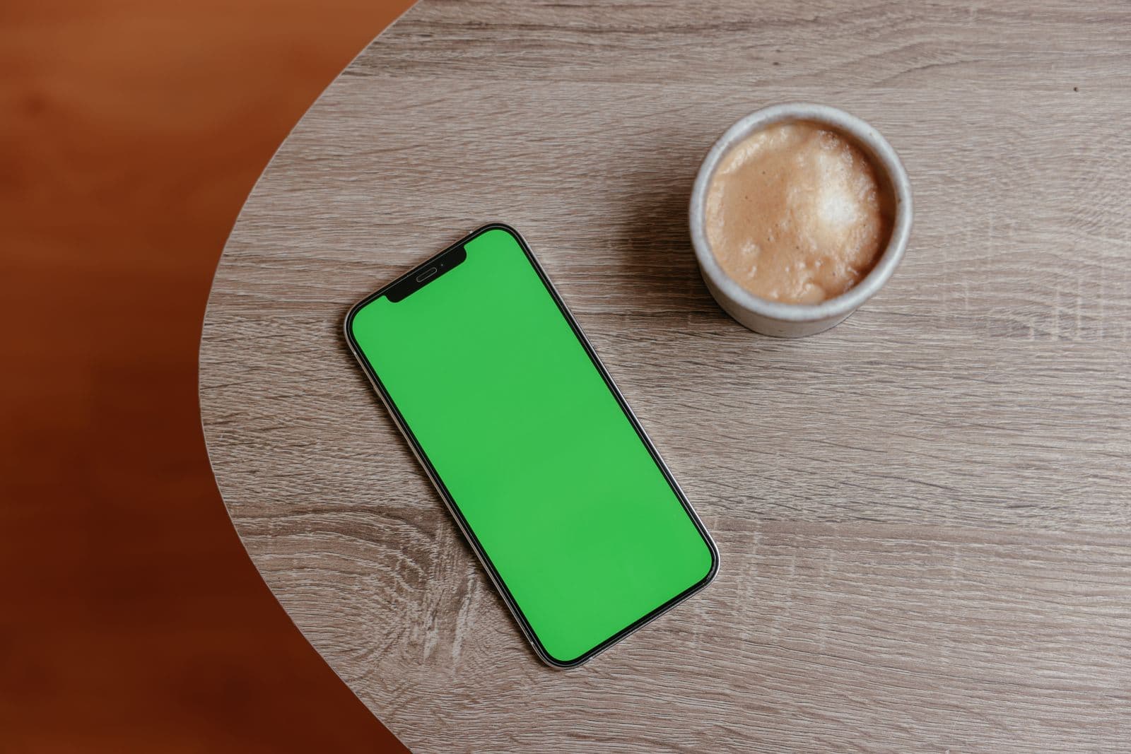 Draufsicht auf ein Smartphone neben einer Kaffeetasse auf einem Holztisch