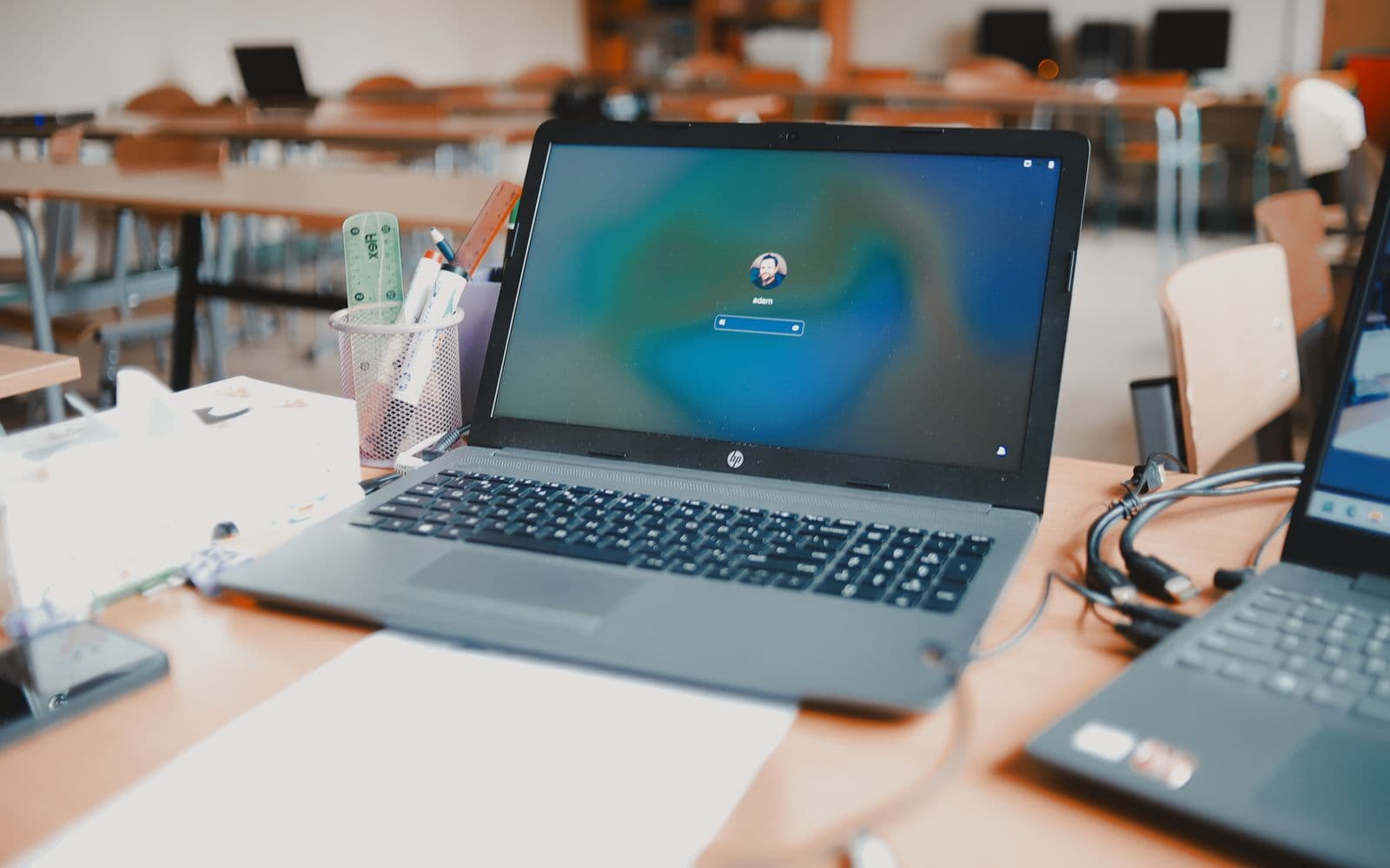 Aufgeklappter Laptop auf einem Tisch in einem Schulungsraum, im Hintergrund weitere Tische und Geräte