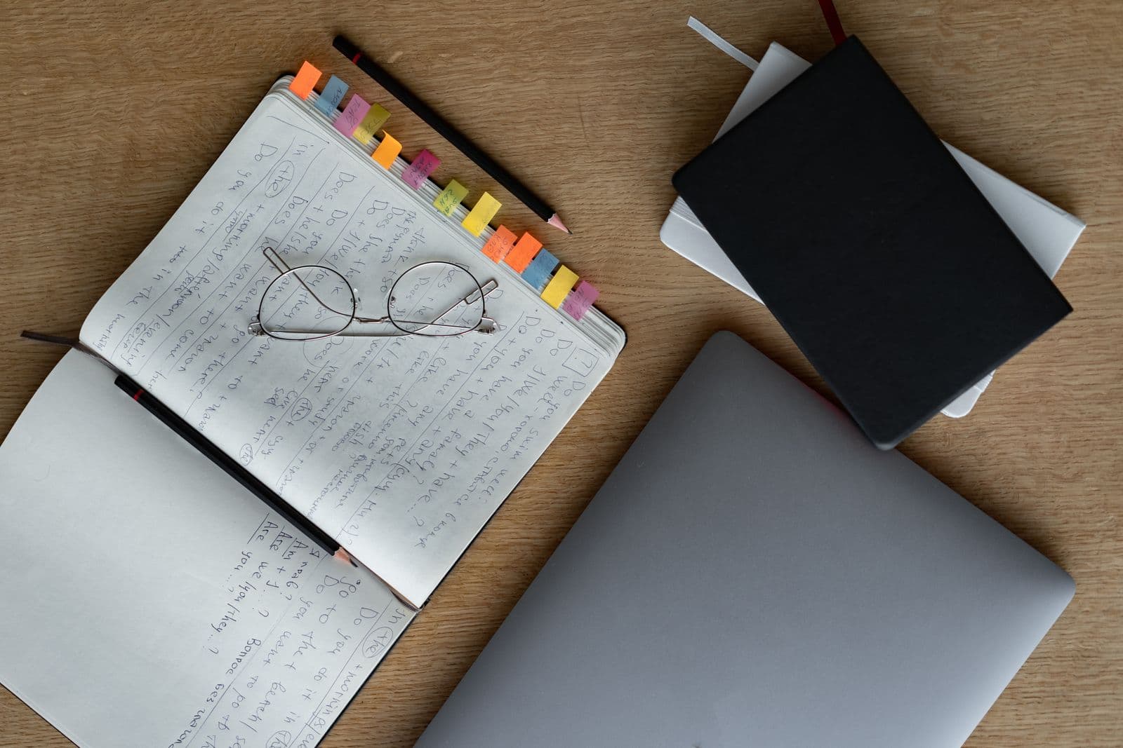 Open notebook with colorful sticky tabs next to a closed laptop and additional notebooks