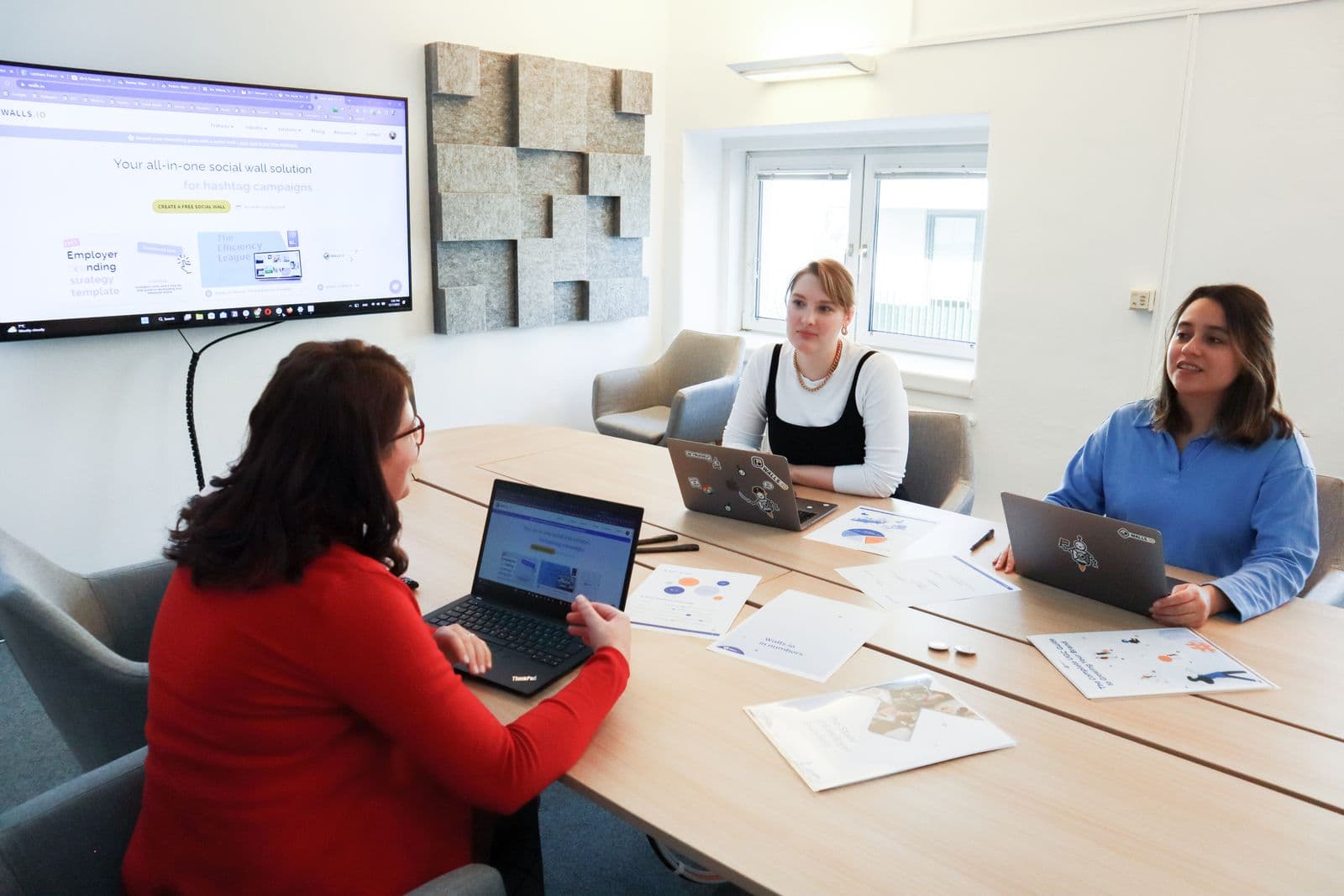 Drei Frauen arbeiten an einem Konferenztisch mit aufgeklappten Laptops in einem modernen Büro zusammen