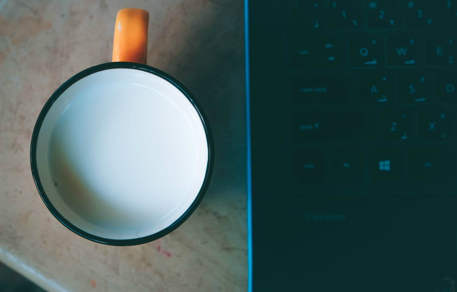 Nahaufnahme von oben auf eine Kaffeetasse neben einer Laptop-Tastatur auf einem Schreibtisch