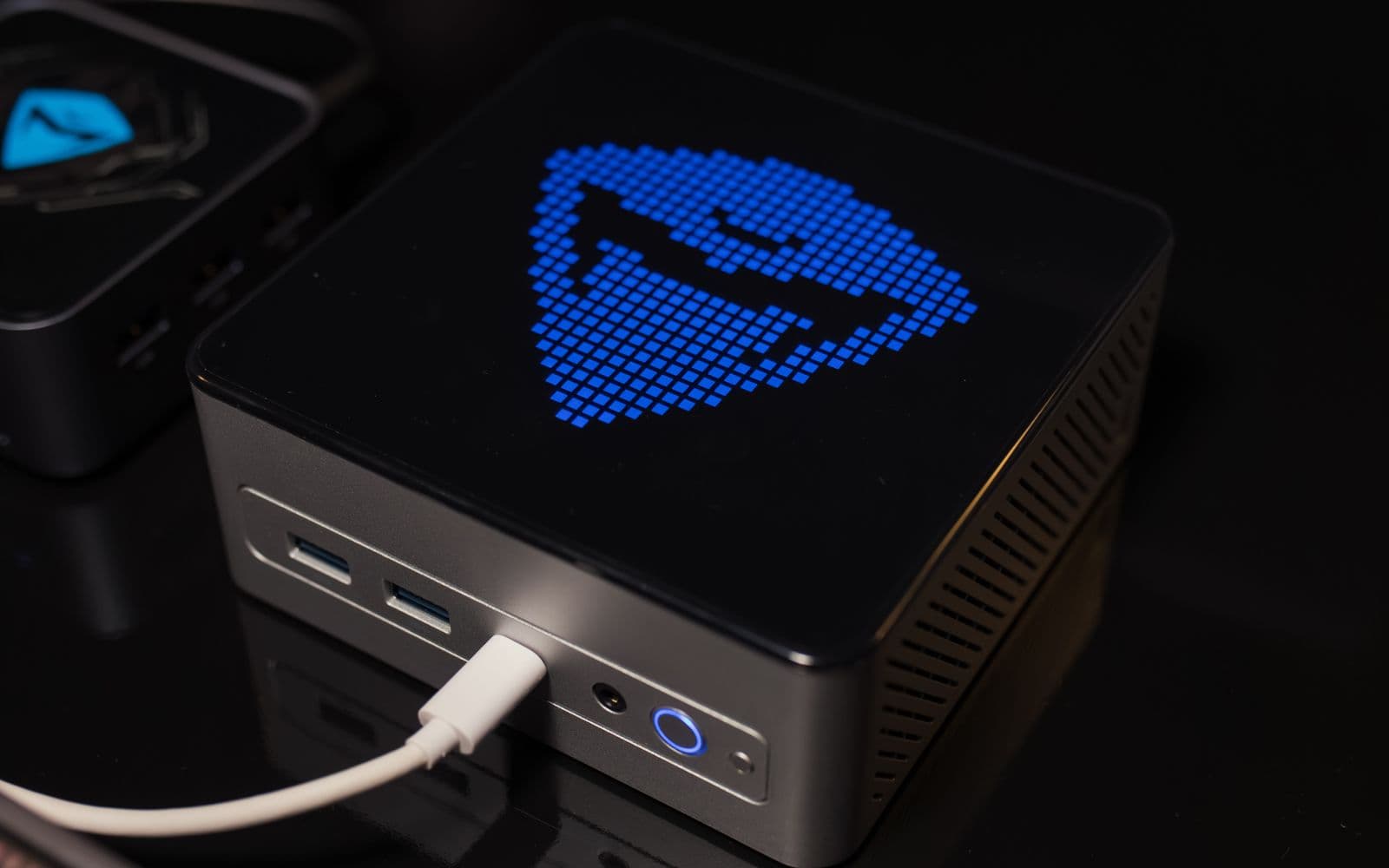 Kompakter Mini-Rechner auf einem Schreibtisch, an der Vorderseite leuchtet eine blaue Punktmatrix-Anzeige