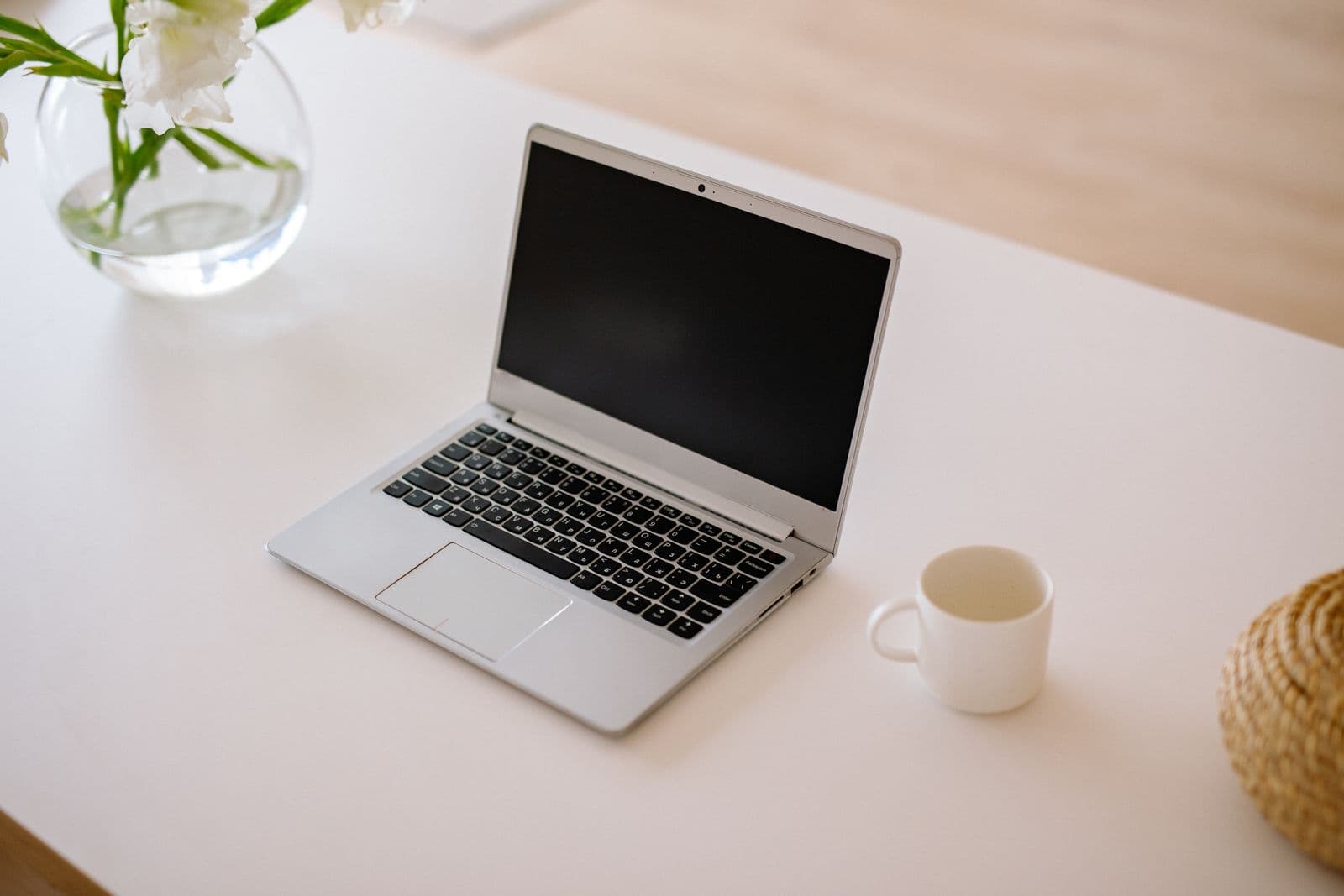 A minimalist workspace with an open laptop, coffee mug and vase on a bright table