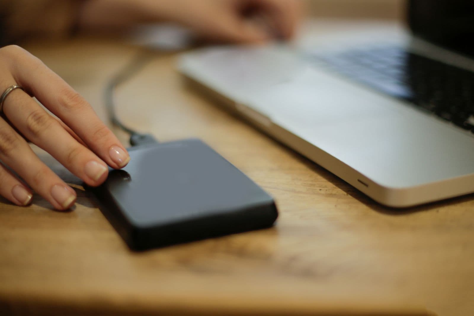 Hand schließt eine externe Festplatte per Kabel an einen Laptop auf dem Schreibtisch an
