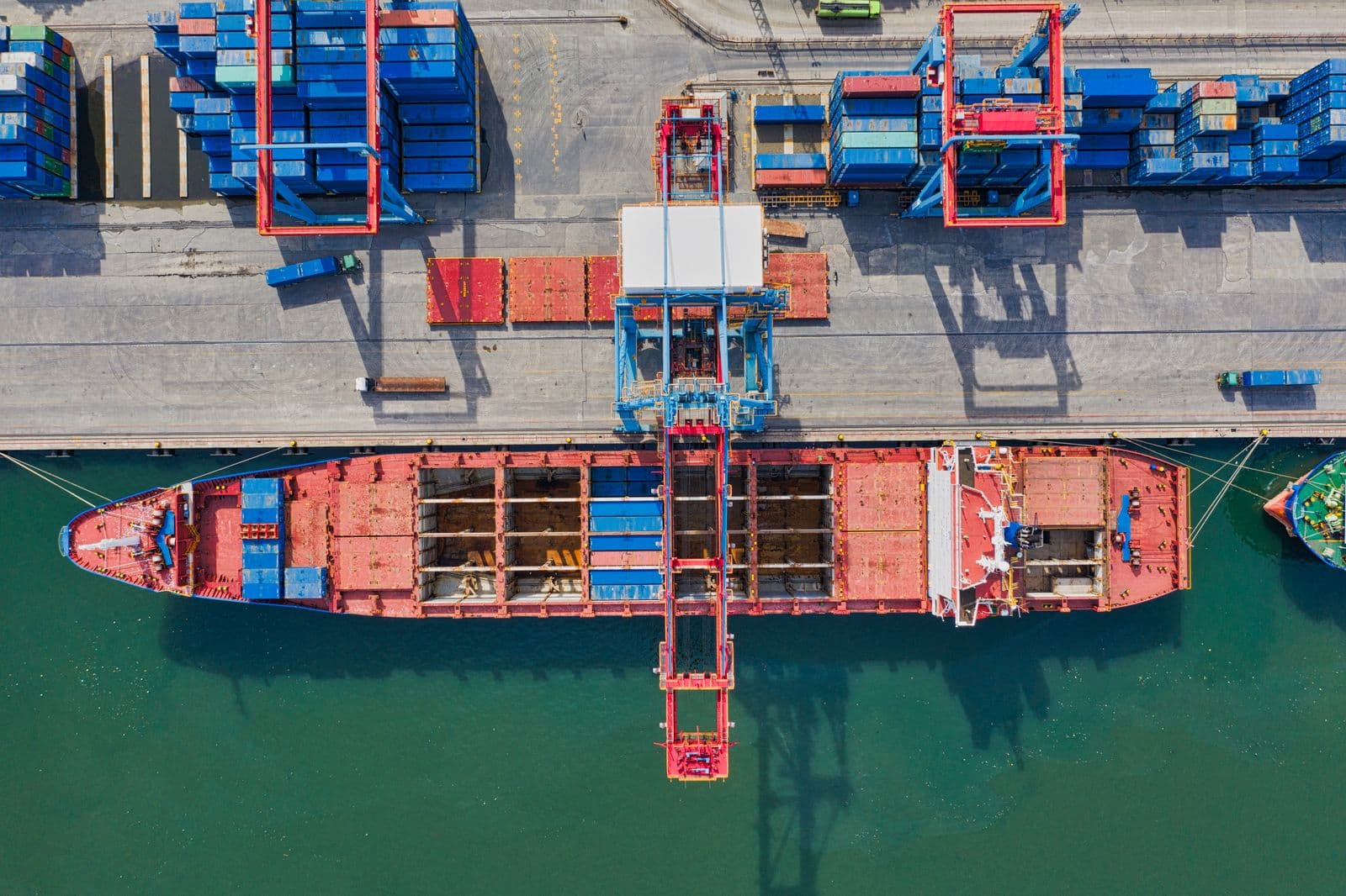 Aerial view of a cargo ship during container handling at the port, a gantry crane moving containers between ship and quay