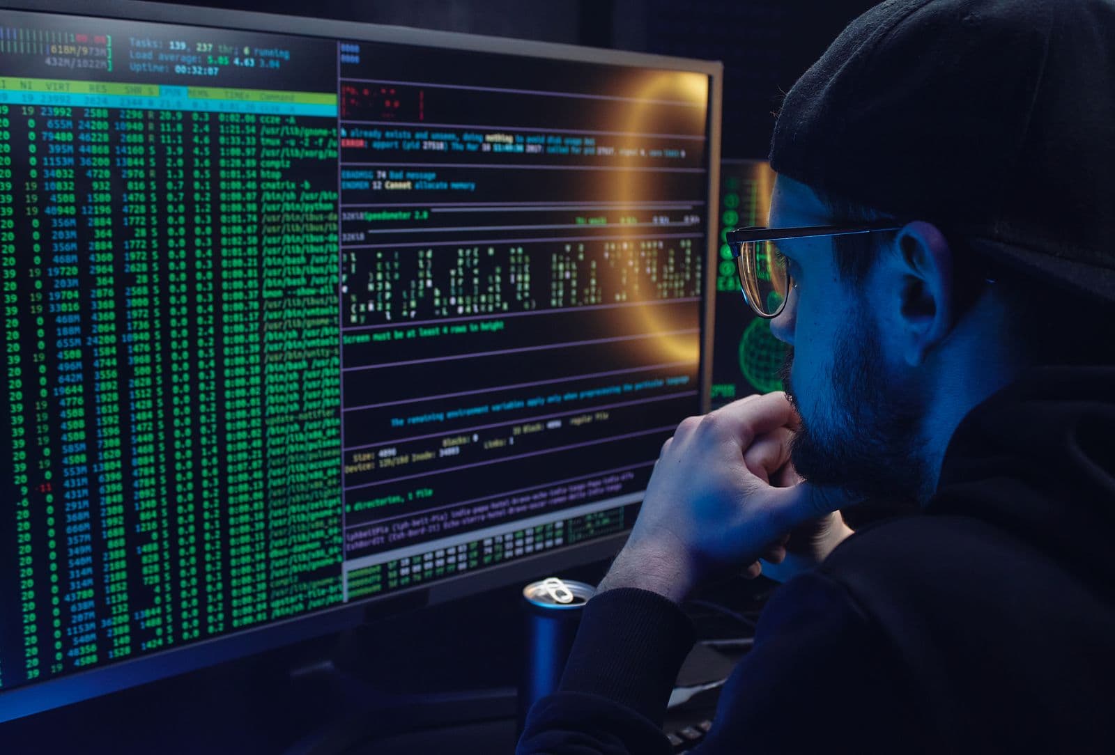 Mann blickt auf zwei Monitore voller Konsolenausgaben und Logzeilen in einem abgedunkelten Raum