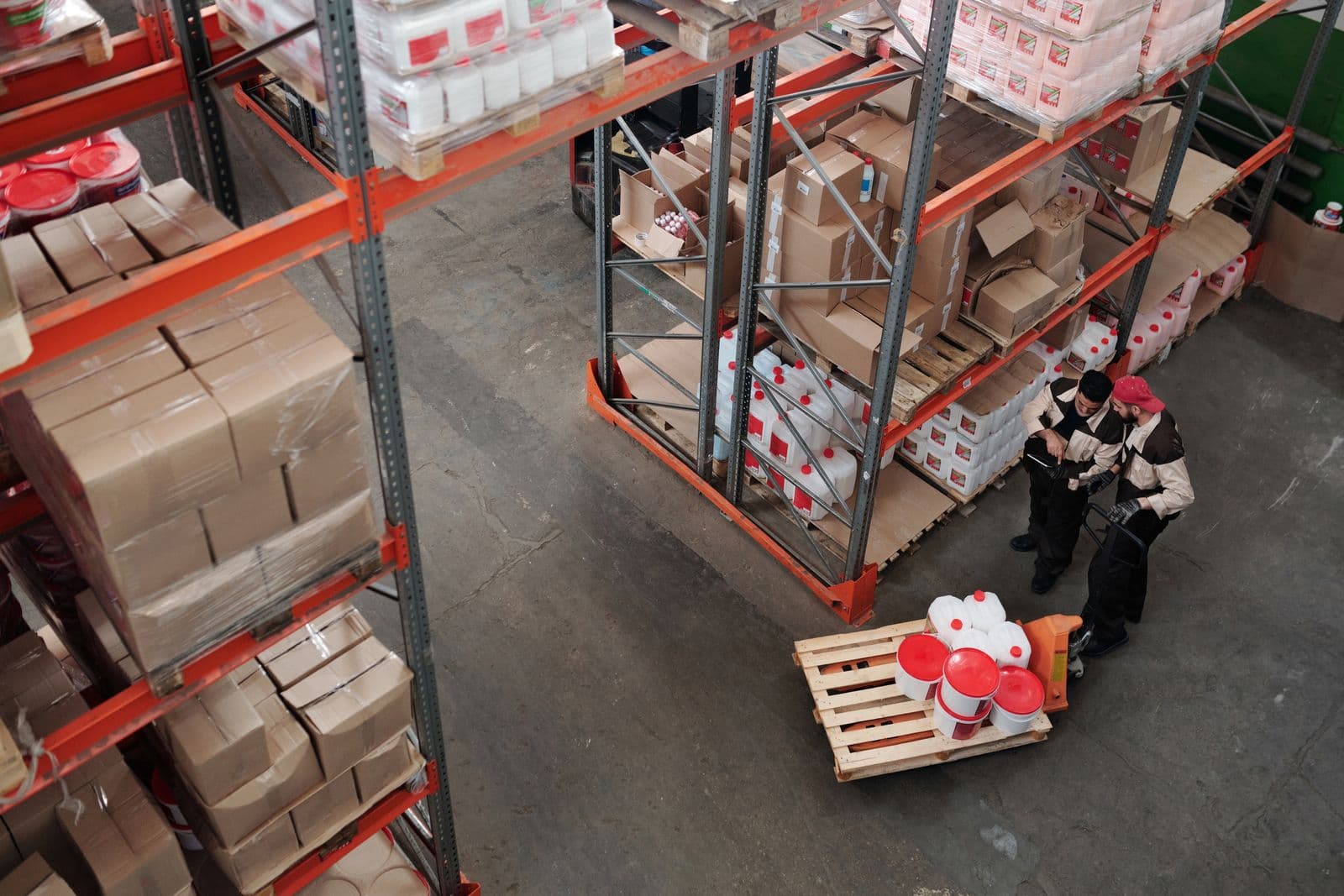 Overhead view of a warehouse, two workers organizing boxes between tall rows of shelving