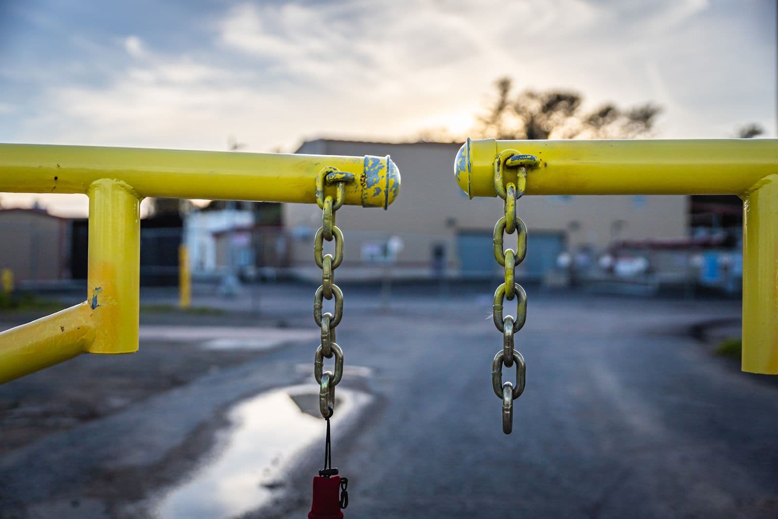 Gelbe Schranke mit zwei herabhängenden Ketten, die eine Industriestraße in der Abenddämmerung versperrt