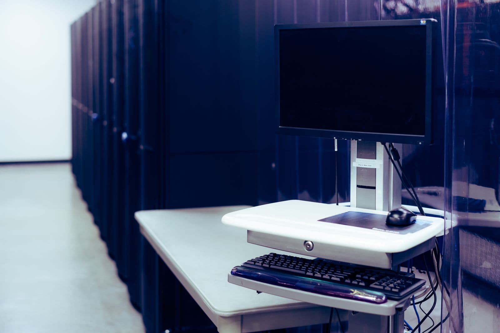 Arbeitsplatz mit Monitor und Tastatur direkt neben einer Reihe von Serverracks im Rechenzentrum