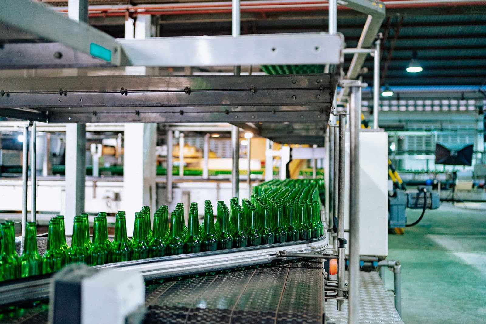 Grüne Glasflaschen laufen nacheinander über ein Fließband in einer Fabrik