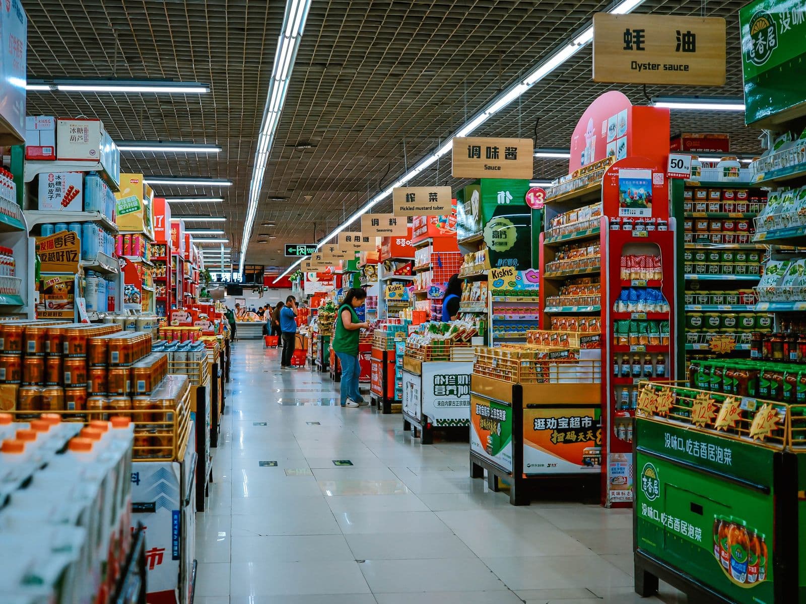 Blick in einen belebten Supermarktgang mit Hinweisschildern über den Regalen