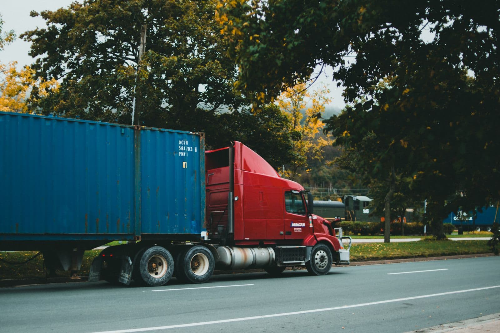 Ein roter Sattelschlepper transportiert einen einzelnen blauen Schiffscontainer auf einer Straße