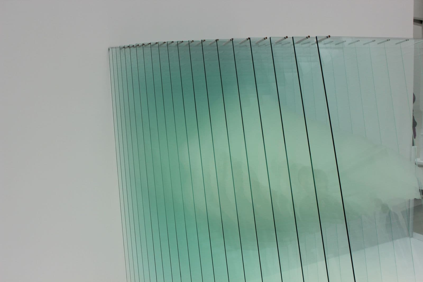 Mehrere transparente Glasscheiben, die hintereinander aufgereiht ein zusammenhängendes Bild mit türkisem Lichtschimmer ergeben