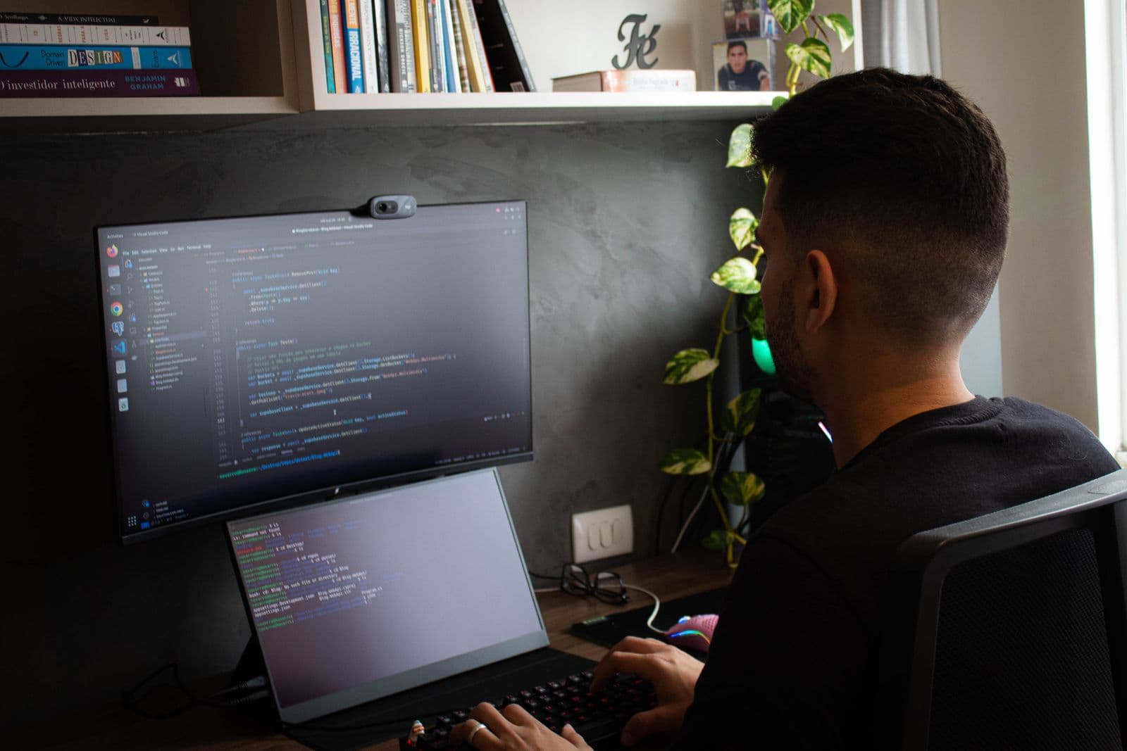 Mann sitzt an einem ruhig beleuchteten Schreibtisch vor einem Monitor mit Code-Editor, darunter ein zweiter kleinerer Bildschirm mit Terminal-Ausgabe