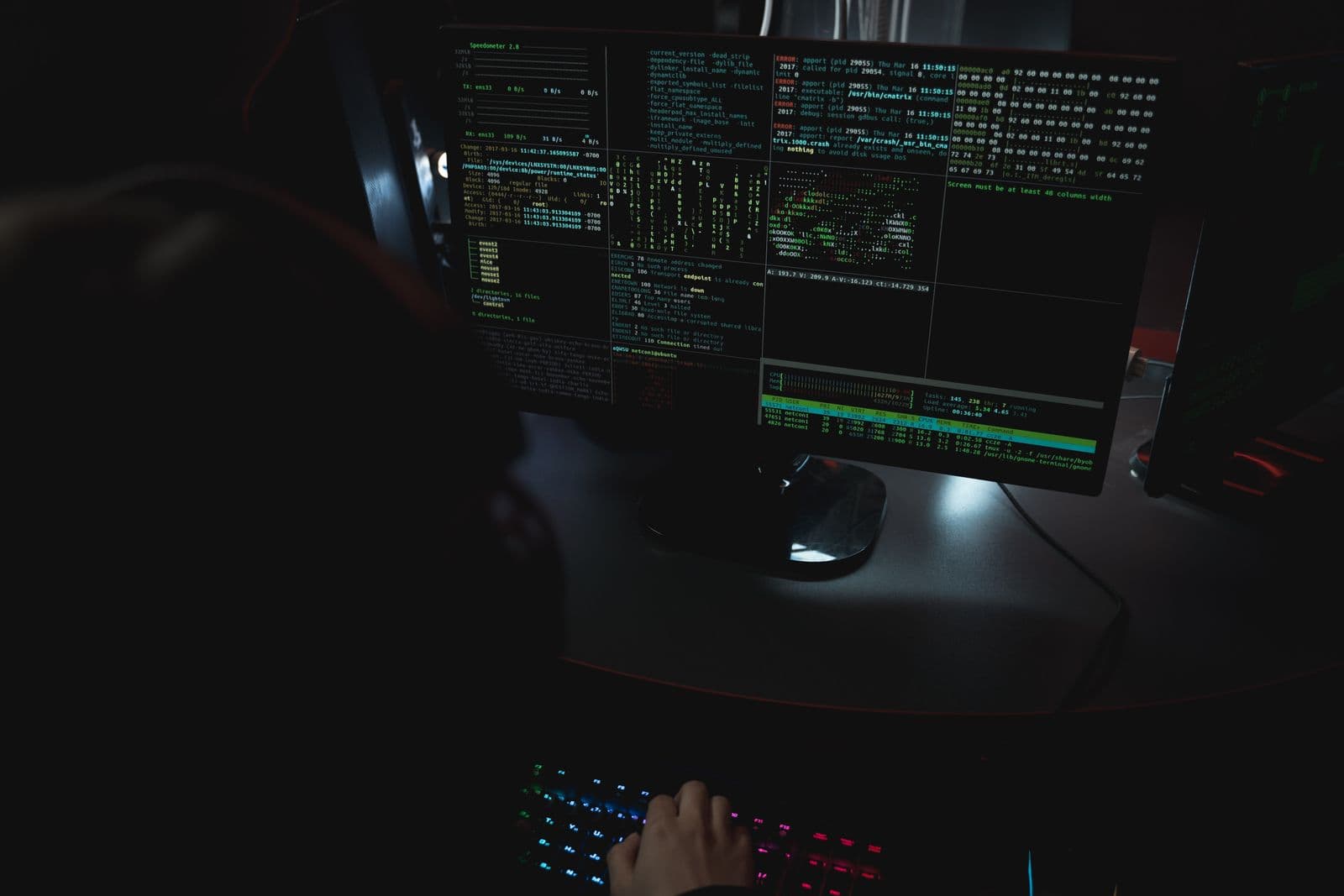 Close-up of a screen showing terminal output and system data, with a hand on a backlit keyboard in front