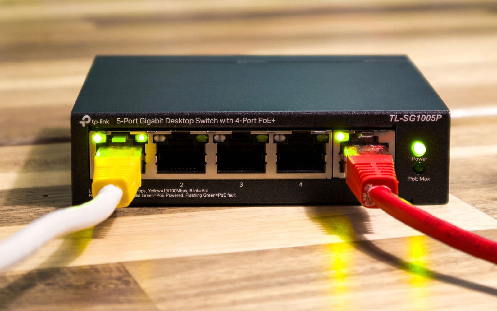 Kleiner Netzwerk-Switch auf einer Holzplatte, zwei Netzwerkkabel sind eingesteckt